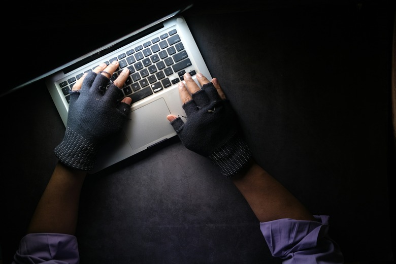 Hands wearing fingerless gloves type on a laptop.
