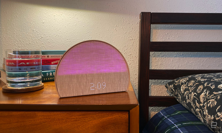 The Hatch Restore 2 sleep machine sits on my bedside table. There's a glass of water and a stack of books in the background. The bed's headboard and pillow are to the right of the image. 