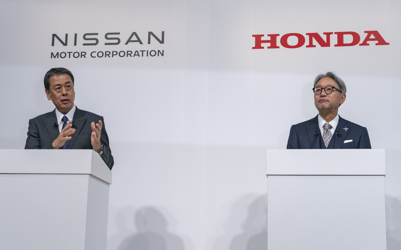 Two men standing behind podiums with the logos of Nissan and Honda in the background.