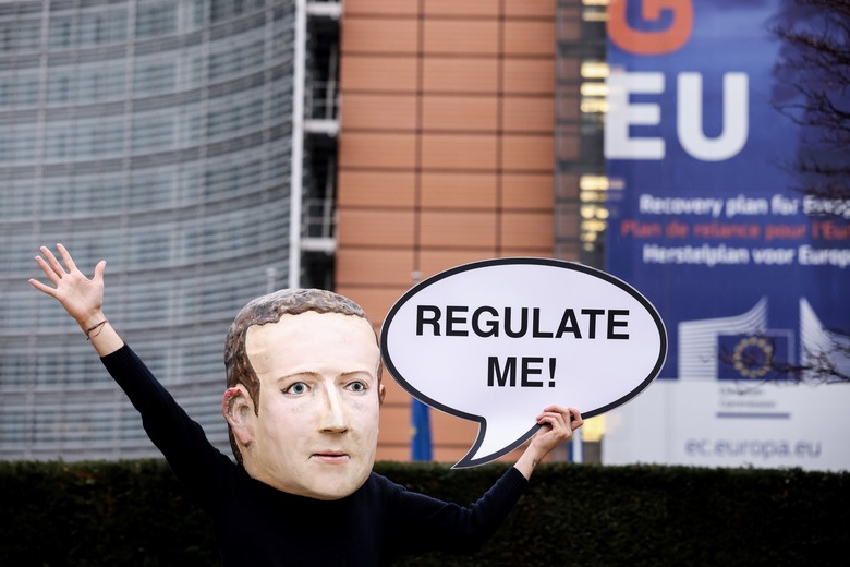 An activist of environmental NGO Avaaz wearing a mask depicting Facebook CEO Mark Zuckerberg holds a banner reading 