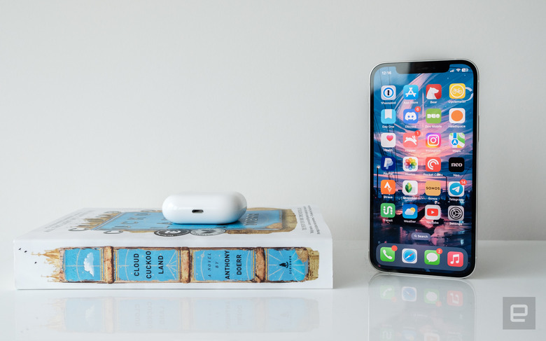 An iPhone 12 next a blue and white book and a pair of AirPods Pro. 