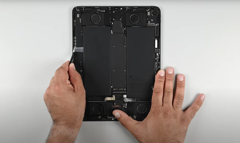 The new iPad Pro with the screen removed, a person's hands are seen holding it and using a tool to access pull tabs beneath one of the battery cells