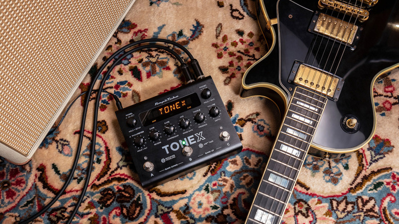 An IK Multimedia ToneX Pedal on very pretty rug next to a black and gold Les Paul. 