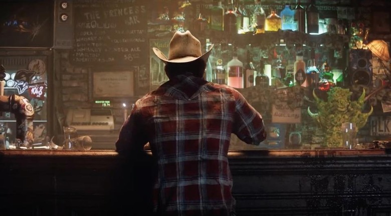 Still from a 2021 teaser for the upcoming ‘Marvel’s Wolverine’ game. Logan is sitting in a dive bar with a cowboy hat and plaid flannel. View from behind with dramatic lighting.