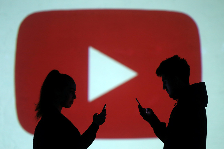Silhouettes of mobile users are seen next to a screen projection of Youtube logo in this picture illustration taken March 28, 2018.  REUTERS/Dado Ruvic/Illustration