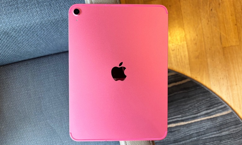 A pink iPad rests on the arm of a chair, with the Apple logo on the tablet's back facing the camera.
