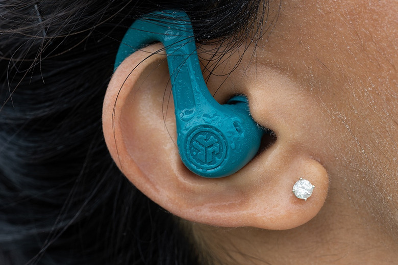 A green-blue earbud with an earhook and water on it is positioned inside a person's ear.