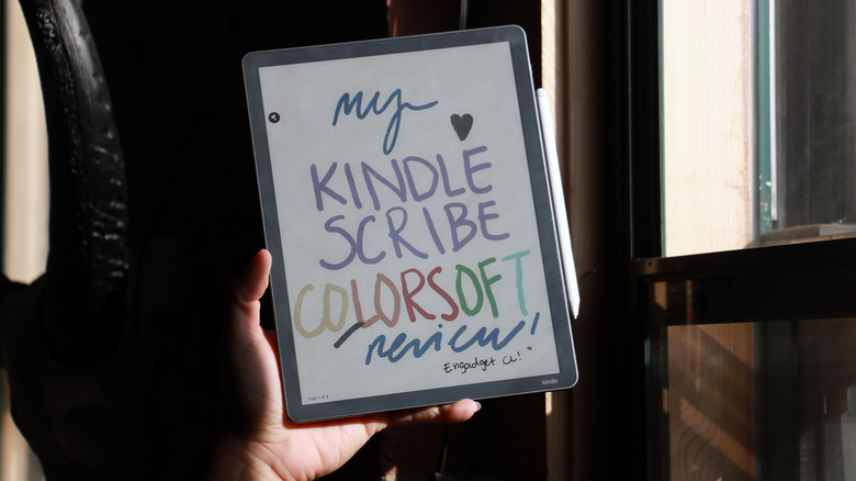 The Kindle Scribe Colorsoft held up in front of a window with sunlight streaming onto its screen, and the words 