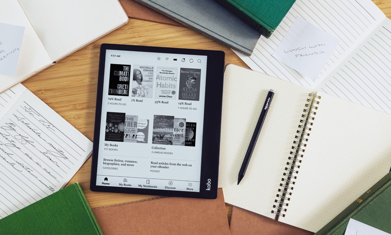 The Kobo Elipsa 2E e-reader on a desk (seen from above), surrounded by its stylus, notebooks and papers. On its screen is a reading library.