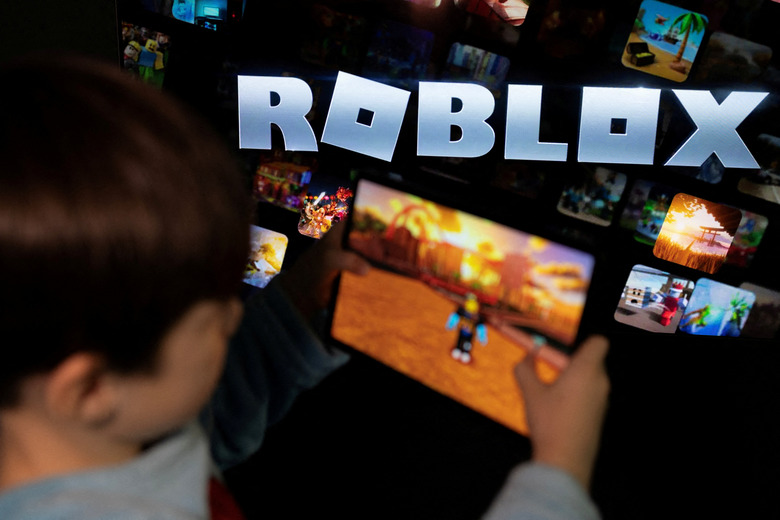 FILE PHOTO: A boy poses for a photo while holding a game pad in front of a screen displaying the logo of the U.S. children's gaming platform Roblox, in this illustration taken December 8, 2025. REUTERS/Ramil Sitdikov/Illustration/File Photo