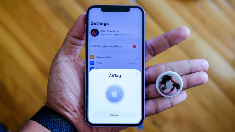 A hand, an iPhone and an AirTag tracker.