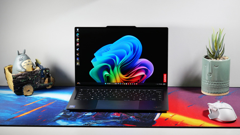 The Lenovo ThinkPad X9-14 Aura Edition on a table with a colorful mat on it, and the laptop's screen shows the Windows 11 home page.
