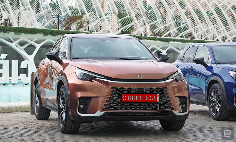 Image of a Lexus LBX parked under the canopy of the City of Arts and Sciences in Valencia. The car is painted in “Sonic Copper,” a sort of metallic orange.  