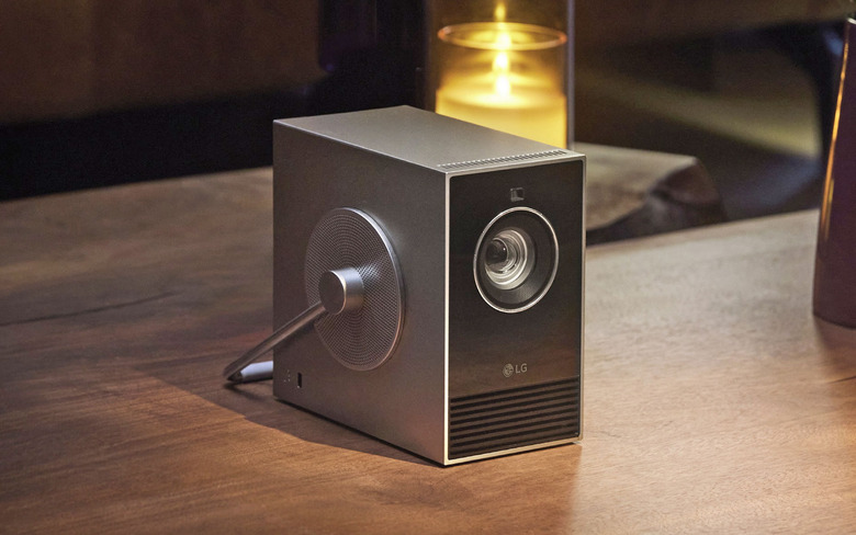 The LG CineBeam Qube projector on a wood table with a candle behind it. 