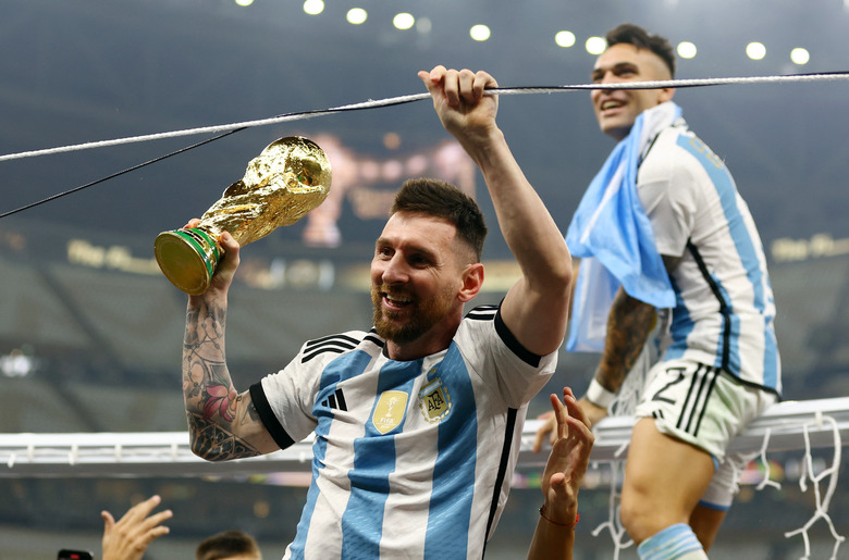 Soccer Football - FIFA World Cup Qatar 2022 - Final - Argentina v France - Lusail Stadium, Lusail, Qatar - December 18, 2022   Argentina's Lionel Messi celebrates winning the World Cup with the trophy as Argentina's Lautaro Martinez is sat on a goal frame REUTERS/Hannah Mckay