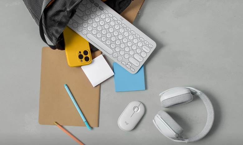 Various items spill out of a bag onto a concrete surface, including a Logitech keyboard, mouse and set of headphones.