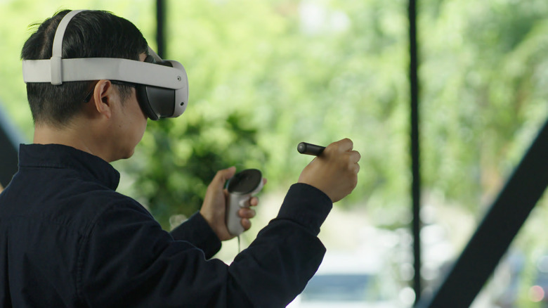 A person wears a Meta Quest headset awhile holding a Quest controller and stylus.