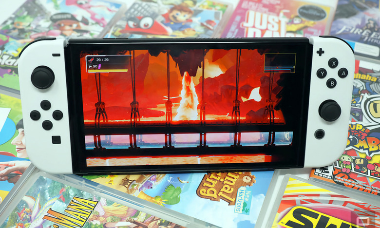 Photo of the Nintendo Switch OLED sitting on a colorful array of game cartridge cases. Its screen shows a fiery scene.