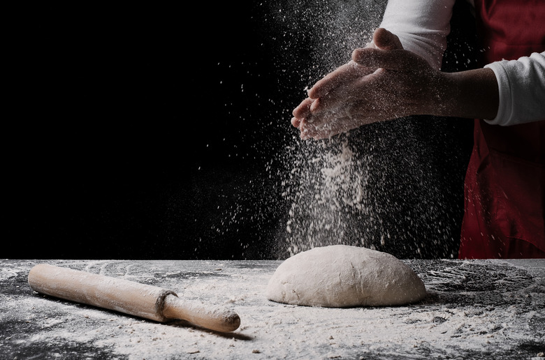 baker preparing bread dough on black table in front of yellow background