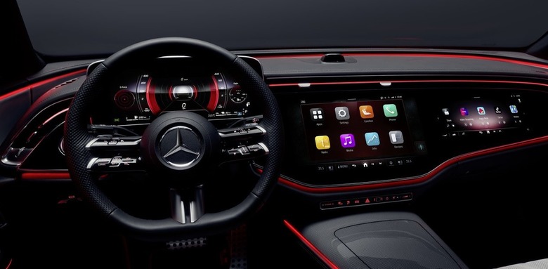 The interior of the Mercedes-Benz 2023 E-Class from the driver's seat, showing the full-width dashboard and red lighting.