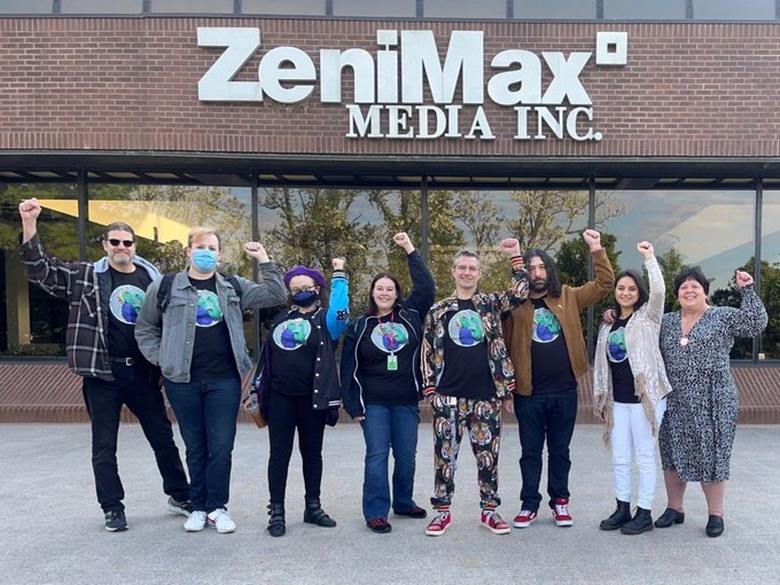 2023 photo of ZeniMax workers standing in a line, raising their fists in unison in front of a ZeniMax Media office.