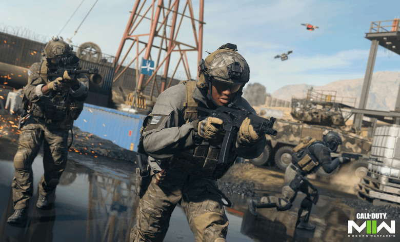 A promo still for the video game 'Call of Duty' showing troops on the ground with weapons up, looking through their sights as they move forward through shallow water in an industrial area.