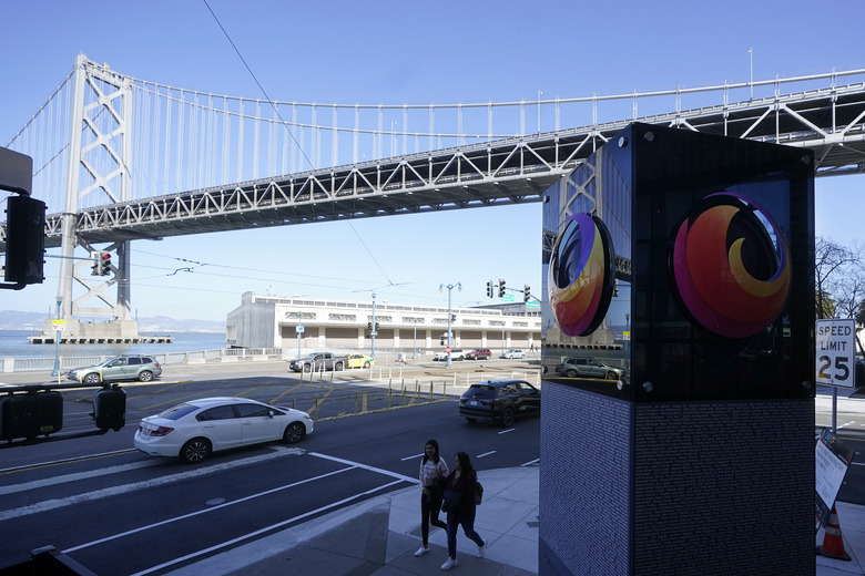 The San Francisco-Oakland Bay Bridge is shown above pedestrians walking next to a Firefox sign at a Mozilla office near the building where a technology executive was fatally stabbed outside of in San Francisco, Wednesday, April 12, 2023. (AP Photo/Jeff Chiu)
