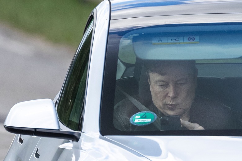 Tesla CEO Elon Musk uses his mobile device as he sits in the car arriving to the construction site for the new plant, the so-called 
