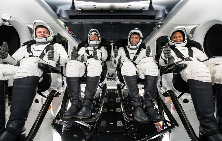 Four astronauts with their space suits on and their thumbs up.