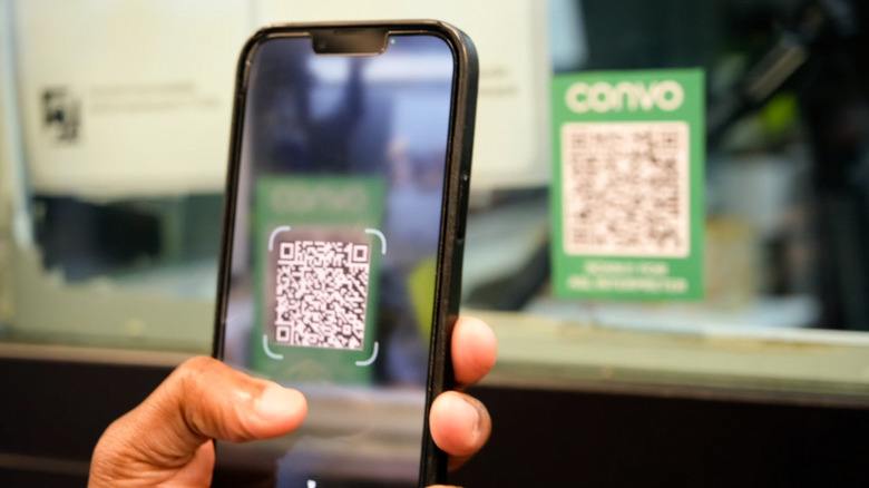 A person holding a phone up scanning a green QR code with the word Convo above it.