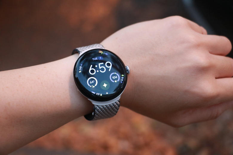 The Pixel Watch 4 on a person's wrist with orange leaves in the background.