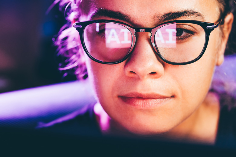 Woman using artificial intelligence technology on laptop with glasses reflection.