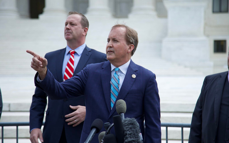 A person in a suit in front of a microphone, pointing at something.