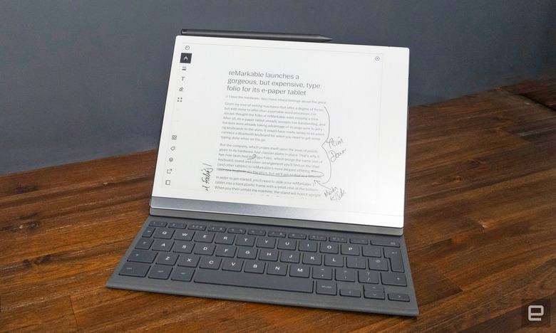 Image of the reMarkable 2 as inserted into its Type Folio keyboard as it sits on a dark wooden table in front of a slate grey wall. 