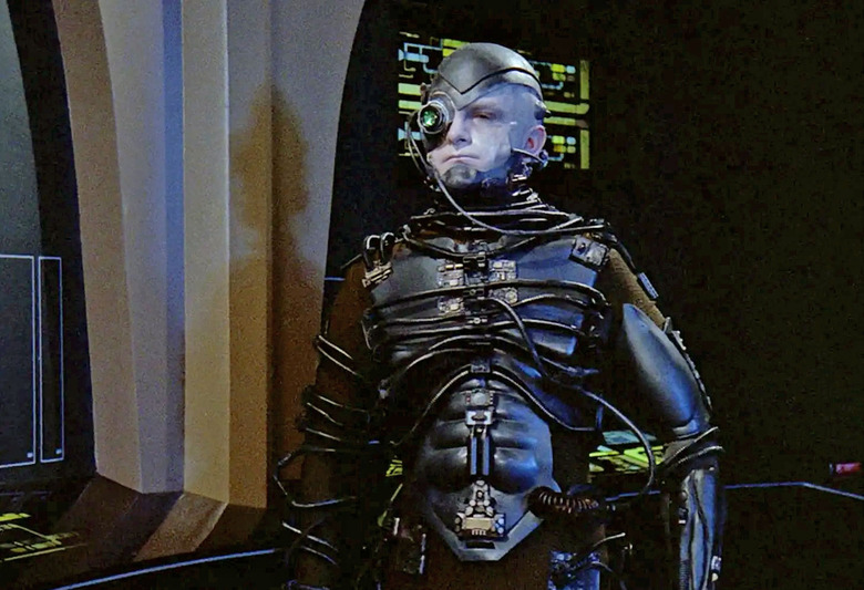 The Borg from Star Trek. A human / machine cyborg stands in a futuristic setting on a spaceship.  