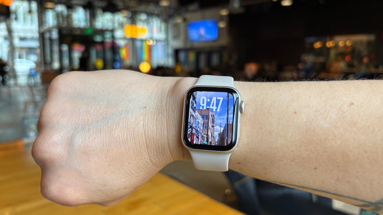 The Apple Watch SE, second generation in 2025 on a person's arm in a coffee shop, showing the photos watch face. 
