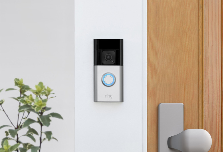 A doorbell with a camera on the wall next to a wooden door.