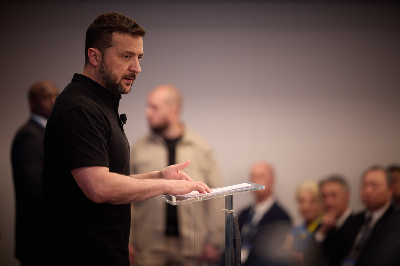 Volodymyr Zelenskyy standing at a podium addressing an audience of government allies.