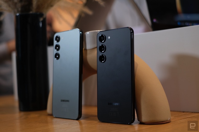 Galaxy S23 and S23+ stood upright on a wooden table, showing the back of the devices.