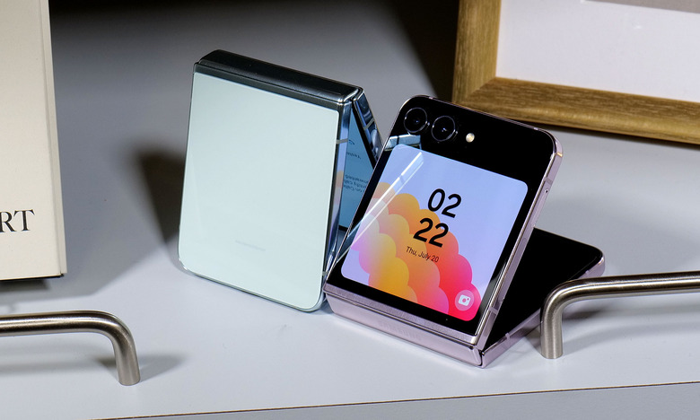 Two Samsung Galaxy Z Flip 5 phones sit on a desk, half-folded and facing opposite directions.