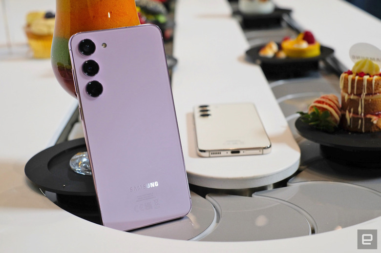 A Samsung Galaxy S23+ smartphone is propped up in the middle of a conveyor belt with food.
