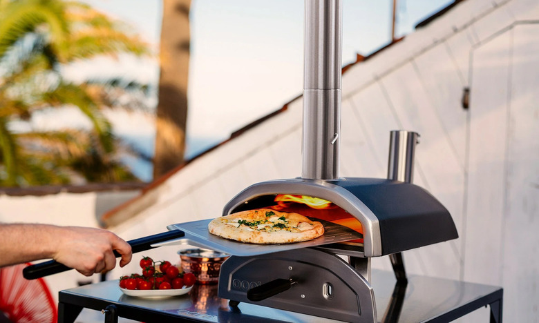 A person takes out a pizza from the fiery depths of the Ooni Frya 12 pizza oven. It looks tasty.