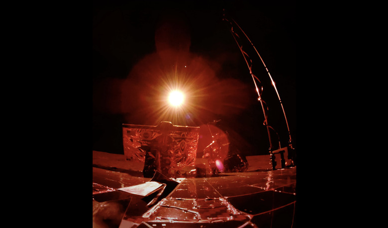 An image captured by Blue Ghost shows a portion of the lander and its solar panel pointed toward the glow of the sun, with a red hue over everything