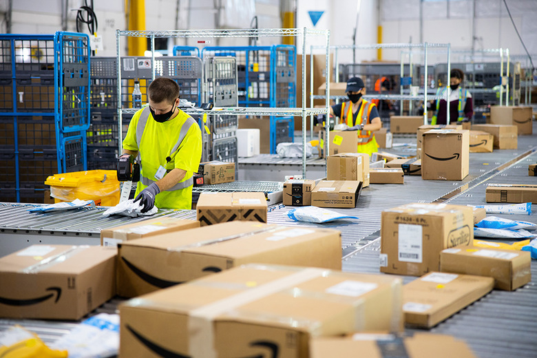 An Amazon warehouse with workers boxing and taping with conveyor belts surrounding them.