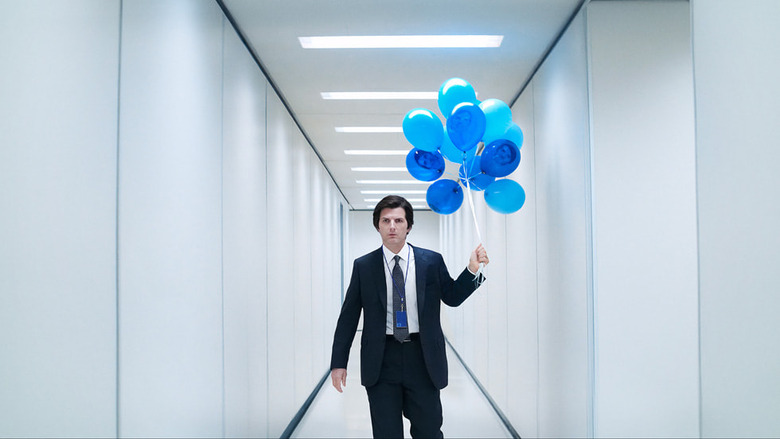 Adam Scott (wearing a suit) holds a bunch of blue blues in a white hallway in Severance.