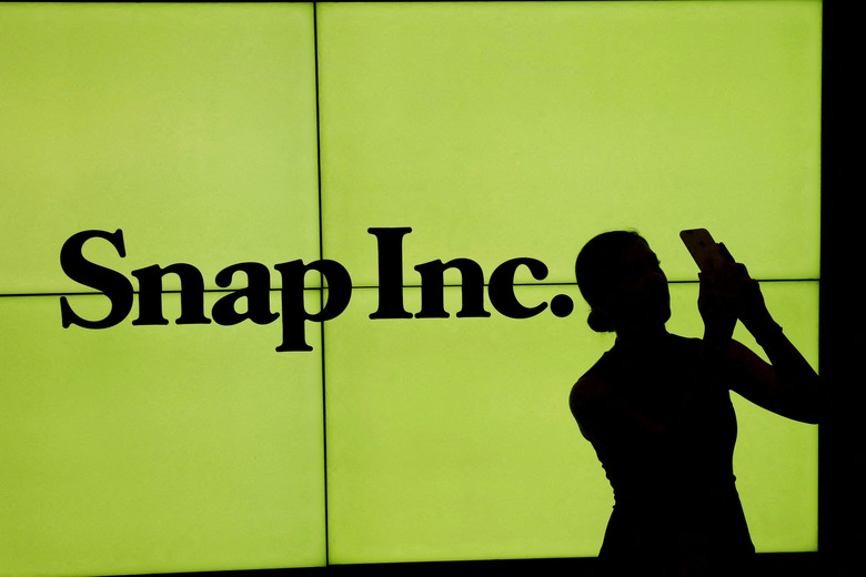 FILE PHOTO: A woman stands in front of the logo of Snap Inc. on the floor of the New York Stock Exchange while waiting for Snap Inc. to post their IPO, in New York City, NY, U.S. March 2, 2017. REUTERS/Lucas Jackson//File Photo