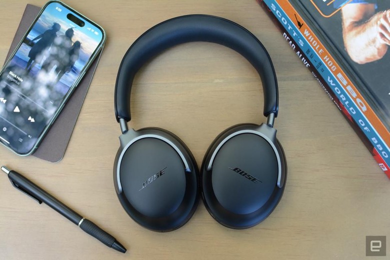 Review photo of the Bose QuietComfort Ultra headphones, sitting on a table next to a pen, phone and books.
