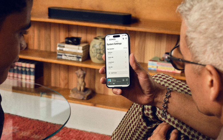 Two people looking at a phone showing Sonos' settings page.