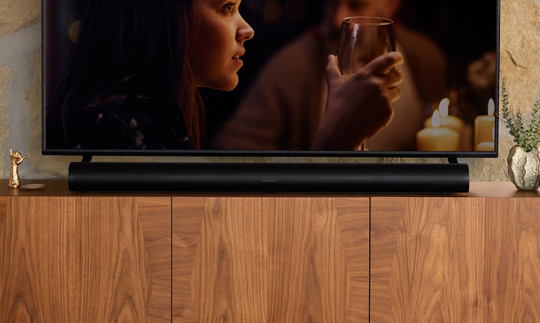 The Sonos Arc sits on a wooden cabinet with a TV above it. 