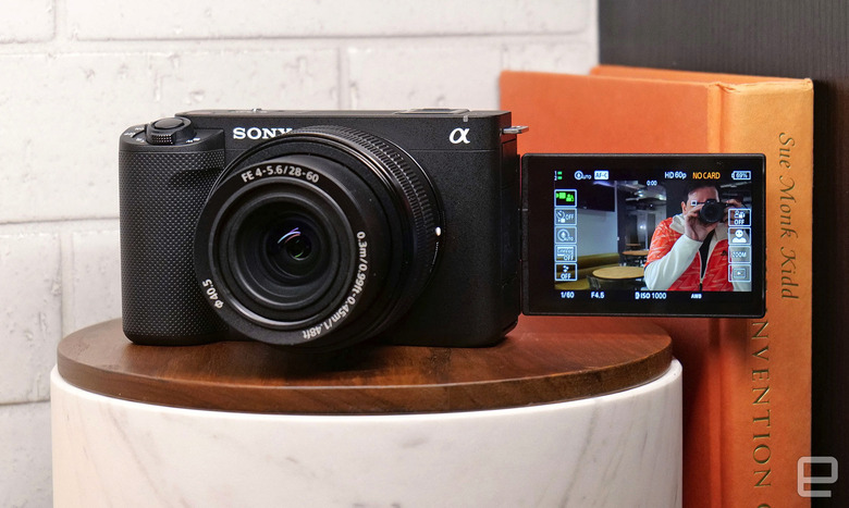 The Sony 12-megapixel full-frame ZV-E1 camera on a cylindrical pedestal next to some books with it's view screen flipped forward to show the person who's taking the photo.